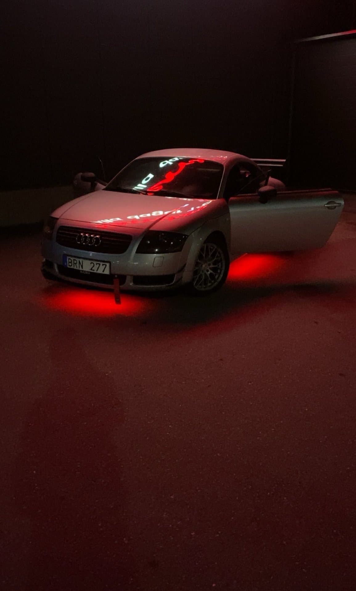 Silverfärgad Audi TT i ett mörkt garage, upplyst av rött ljus underifrån.