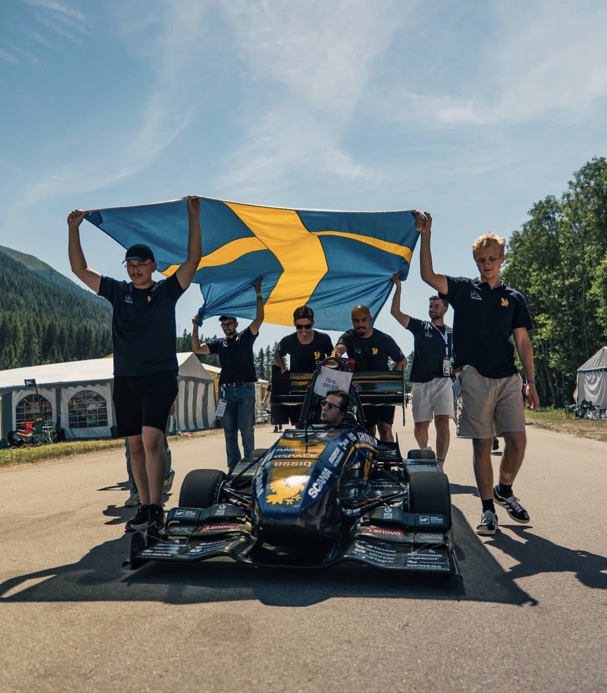 Teammedlemmar håller upp en svensk flagga bakom bilen på FSCH.