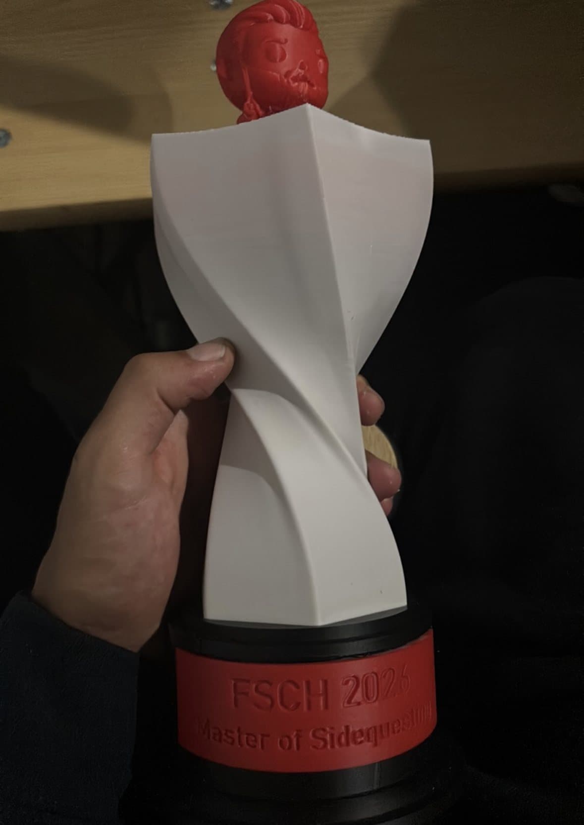 Vit vriden pokal med ett rött huvud på toppen och texten FSCH Master of Sidequesting.