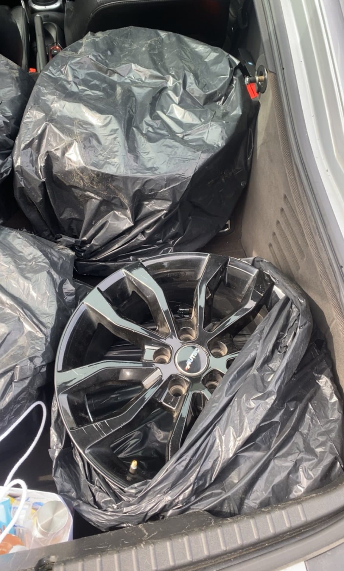 Svarta femekrade fälgar i plastsäckar i en bil.